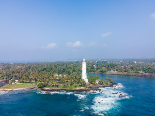 Aerial drone photo of Dondra Head Lighthouse viewed from the sea on a bright sunny day, Sri Lanka. Tall white lighthouse standing on the southernmost point of the island, surrounded by deep blue ocean
