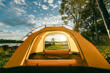 A cozy yellow camping tent pitched on lush green grass by a peaceful lakeside during golden hour. nature travel, and serene outdoor living. Ideal for themes of camping, weekend getaway,