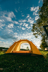 A cozy yellow camping tent pitched on lush green grass by a peaceful lakeside during golden hour. nature travel, and serene outdoor living. Ideal for themes of camping, weekend getaway,