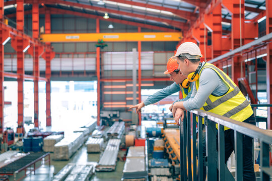 Caucasian industrial engineer men wear safety helmet vest standing on elevated catwalk supervising factory floor. Manager partner pointing future vision in manufacturing plant. Heavy metal industry