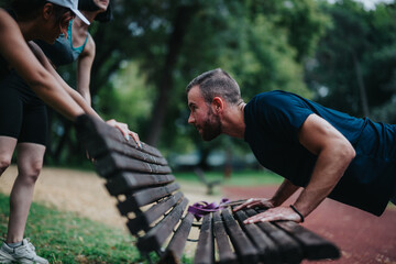 Outdoor fitness scene with adults pushing a bench in a park. A group exercises together, using a bench for strength training.