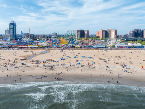 Aerial view of sunbathers speckle the golden beach, the iconic Wonder Wheel and Cyclone roller coaster stand silhouetted against the skyline, Brooklyn, New York, United States.
