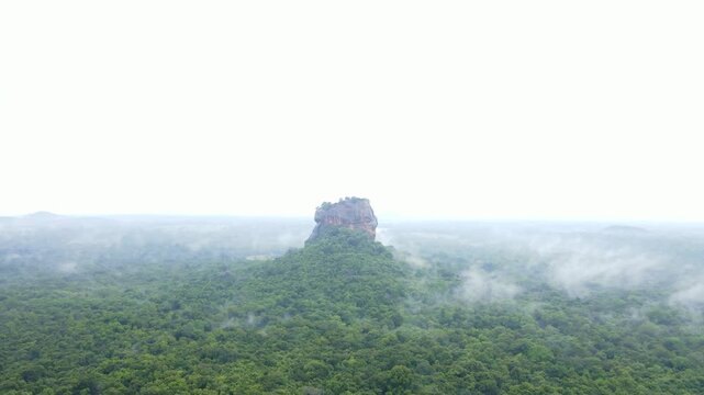 Early morning aerial drone footage of Sigiriya Rock Fortress after rain, Sri Lanka. Low clouds and mist drifting above lush tropical jungle, with wet surfaces reflecting soft morning light.Atmospheric