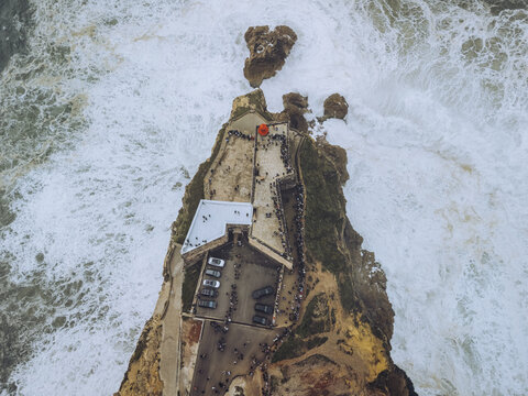 Aerial view of the Fortaleza de Nazar&eacute; perched dramatically on a cliff, engulfed by the turbulent Atlantic waves, a striking contrast of earth and sea, Nazar&eacute;, Leiria District, Portugal.