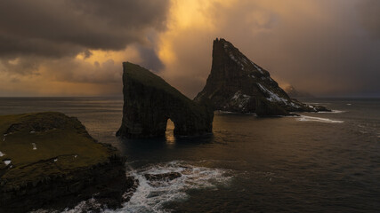 Aerial view of the Drangarnir sea stack and Tindholmur islet stand majestically against a dramatic sky, their rugged forms contrasting with the surrounding ocean, Vagar, Vagar, Faroe Islands.