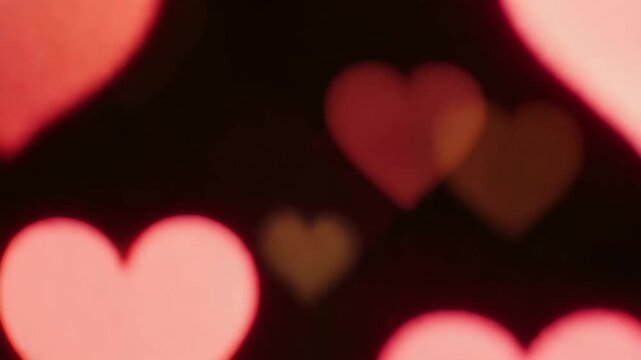 Colorful heart-shaped blurred bokeh on black background. Abstract lights loop. New year and Christmas. Shimmering glittering particles with bokeh. 4K, vertical video, social media