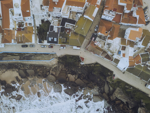 Aerial view of the rugged coastline meeting the charming town with white buildings and terracotta roofs, a stunning contrast of nature and architecture, Ericeira, Lisbon, Portugal.