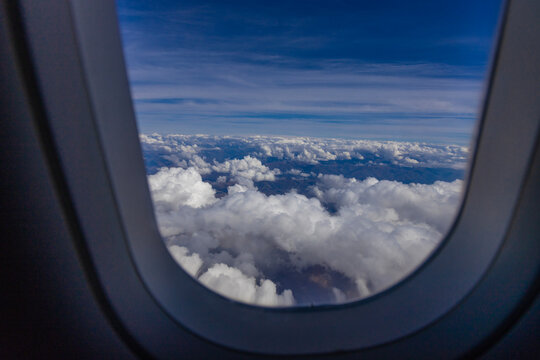 Cloud layers in the sky seen from airplane window with wing edge, aerial travel perspective, white cumulus and cirrus formations above landscape, aviation altitude view, weather patterns, daylight fli