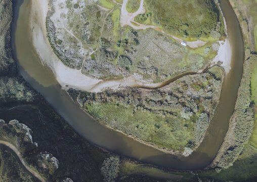 Aerial view of the serpentine river curves dramatically through the landscape, showcasing a blend of earthy tones and vibrant greens, Foz do Lizandro, Ericeira, Lisbon, Portugal.