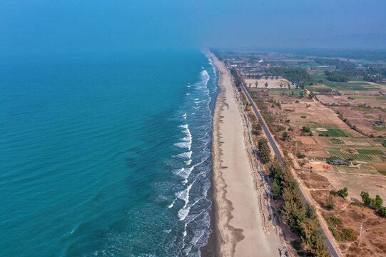 Aerial view of the sandy beach meeting the turquoise sea, a coastal road running parallel to the shore and buildings, Cox's Bazar, Chittagong Division, Bangladesh.