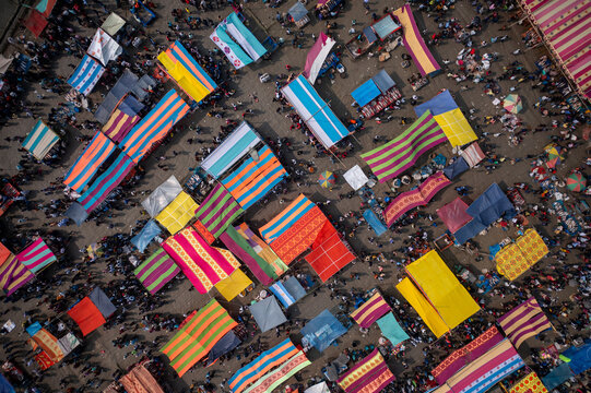 Bogura, Bangladesh - 10 February 2021: Aerial view of a vibrant, bustling marketplace, where colorful striped awnings create a patchwork of light and shadow above the crowded scene.