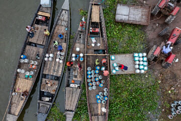 Sirajganj, Bangladesh - 12 July 2020: Aerial view of boats laden with goods meet tractors ashore, a vibrant scene of commerce amidst the green vegetation.