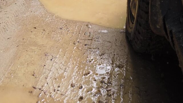 Car splashes through muddy puddles along a rural road, causing mud to fly as it accelerates off the beaten path in an exhilarating display of off-road fun