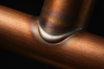 Heat-Treated Copper Pipe Joint With Brazed Seam And Oxidation Colors On Dark Background
