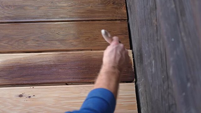 Brown oil for protection of wood by staining. Painting a larch for protecting and pests. Woodworker applying finish to terrace deck board. Repairman varnishing with brush wooden plank floor surface.