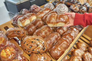 Female hand holding wrapped bread loaf in bakery display with various pastries.