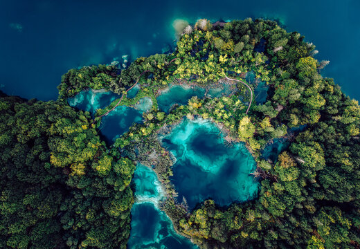 Aerial view of a vibrant, turquoise lake nestled among a tapestry of emerald and jade forests, Plitvicka Jezera, Lika-Senj County, Croatia.