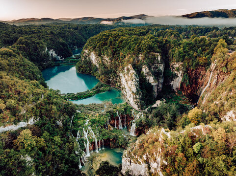 Aerial view of cascading waterfalls spill into turquoise pools amidst lush green forests and towering cliffs, Plitvicka Jezera, Lika-Senj County, Croatia.