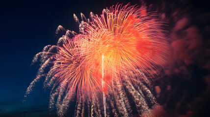 Spectacular orange and red fireworks burst brightly across the dark night sky during a festive celebration