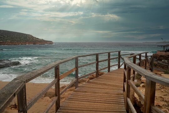 panorama con molo di legno per accesso alla spiaggia con sfondo di mare mosso e cielo nuvoloso con temporale in arrivo