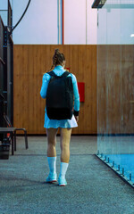 Female athlete walking backwards with a backpack entering or leaving a padel club for training.