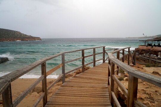 Primo piano di passerella per accesso alla spiaggia con mare ondoso color turchese cielo nuvoloso con tempesta in arrivo 