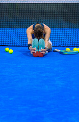 Athlete performing forward hamstring flexion stretches on a blue padel court in front of a net.