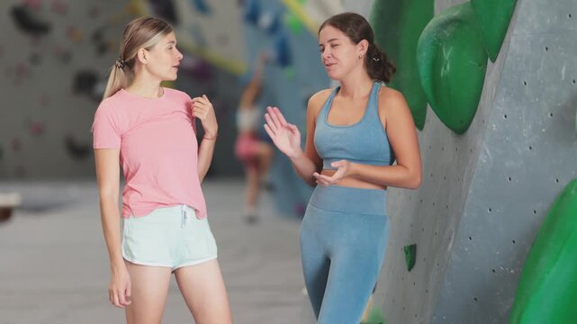 Two female friends in climbing gym hall, having nice conversation before training, discussing workout plan and sharing fitness tips. High quality 4k footage