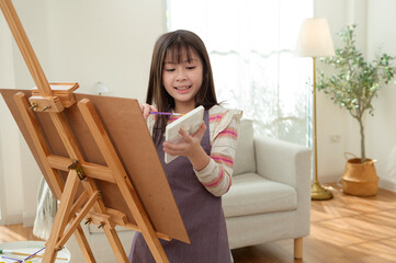 Child Creates Art While Standing at an Easel in a Bright Room During Daytime