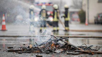 Close-up of a smoldering fire with smoke and embers. Firefighters in the background during an emergency response or safety training