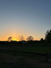 Rural Sunset Landscape With Fence and Trees.
Peaceful rural landscape at sunset with wooden fence, grass field and tree silhouettes under colorful evening sky.