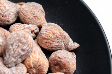 Dried fig dusted with powdered sugar on black ceramic dish close up