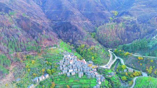 Piodao historic schist village in autumn and Serra do Acor mountain slope with lush green and burned vegetation scorched by forest fires. Central Portugal. Aerial view. Orbiting