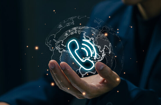 A glowing phone icon over a digital globe in a professional hand represents global communication, call center support, customer service, international business, and telecom technology. - Powered by Adobe