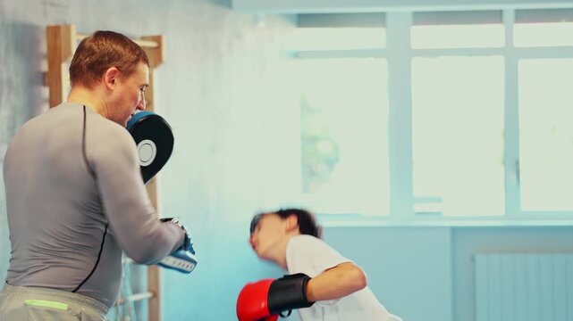 Active teen male practitioner of boxing courses applying kicks on hitting mitts during workout session