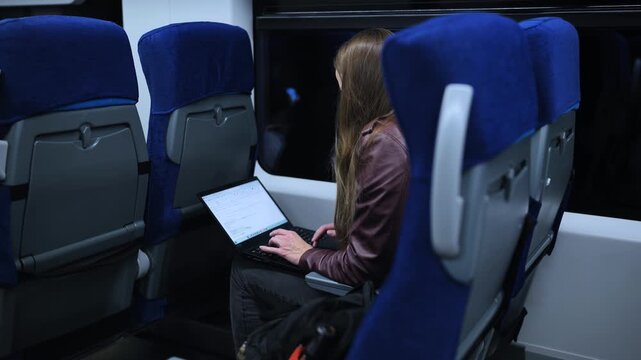 Woman working remotely with her laptop computer while commuting on a train at night