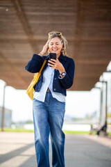 Smiling mature woman using smartphone while walking outside