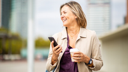 Happy older woman looking aside holding coffee and phone