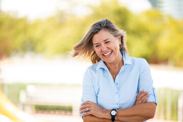 Cheerful mature woman smiling with arms crossed on a sunny day