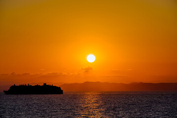 Silhouette of a cruise ship at sea during an orange sunset sky over the horizon	
