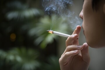 Fototapeta premium Asian young adult male smoking cigarette outdoors with green background