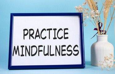 Mindfulness symbol. Concept words Practice Mindfulness on beautiful wooden picture frame. Beautiful light blue background with flower vase. Medical and Psychology concept. Copy space.
