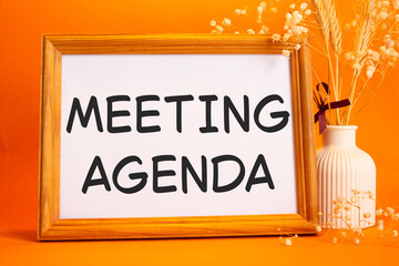 Meeting agenda symbol. Concept words Meeting agenda on beautiful wooden picture frame. Beautiful orange background with flower vase. Business and Meeting agenda concept. Copy space.