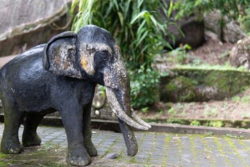 Fototapeta premium A weathered elephant statue stands in a lush, green garden setting.