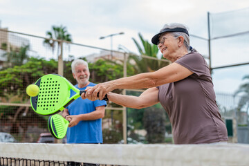 Portrait of couple of mature people playing padel game outdoors in a paddle tennis court together. Old man and mature woman teammate having fun enjoying