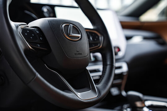Close up interior view shows Lexus RX 450h Plus wheel with L emblem and SRS Airbag, multi function controls, large touchscreen, soft touch trim, and soft natural light.