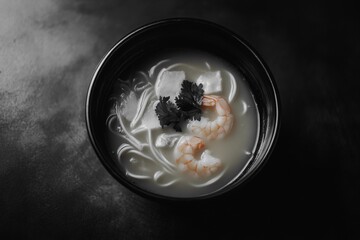 A bowl of delicious, warm soup with noodles and shrimp, topped with seaweed.