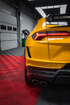 Tight three quarter rear view shows a Yellow Lamborghini Urus Performante parked indoors on a red and black checkered workshop floor with LED taillight, quad tips, diffuser, and aero wing visible.