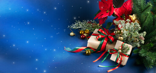 Christmas banner with gift boxes with bow, red poinsettia, decorative fir branch, bells and balls for tree decoraton on blue background. New Year winter holiday decor composition with presents.