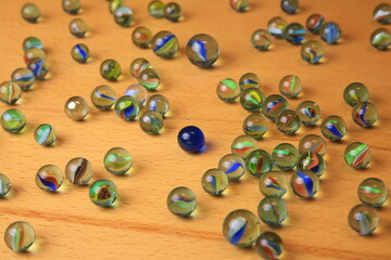 Bunte Glasmurmeln mit farbigen Wirbeln liegen verstreut auf Holz. Eine dunkelblaue Vollmurmeln hebt sich deutlich ab und symbolisiert Individualität inmitten der Vielfalt.